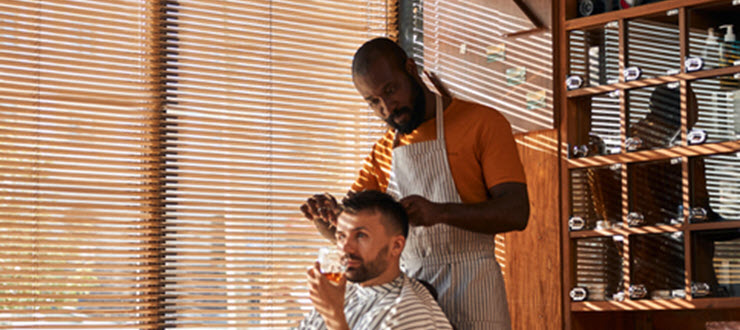 Man getting haircut by barber with liquor drink in hand