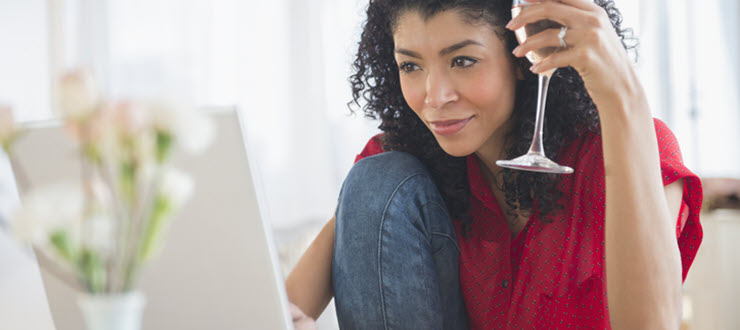 Woman with wine glass taste testing in front of laptop